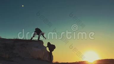 在两个登山者之间帮忙的剪影。 山顶上有两个徒步旅行者，一个人帮助一个人爬上一个纯粹的地方